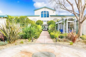 A building with a central entrance, surrounded by a garden with various plants and a pathway leading to the entrance. - Napa 2BR condo at Silverado Resort — two king suites, golf views (Napa)