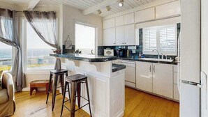 A modern kitchen with white cabinets, a marble countertop, and a view of the ocean. - Bodega Bay 2BR oceanfront cottage above Carmet Beach — dog friendly (Bodega Bay)