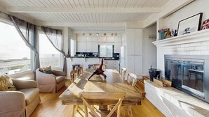 A modern living room with a wooden dining table, sofas, a fireplace, and a kitchen in the background. - Bodega Bay 2BR oceanfront cottage above Carmet Beach — dog friendly (Bodega Bay)