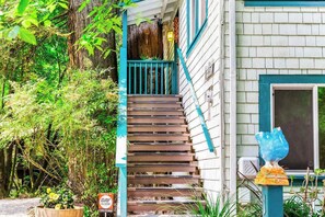 A wooden staircase leading to a porch with a blue railing, surrounded by lush greenery. - Guerneville Dog-Friendly Redwood Retreat with Deck (Guerneville)