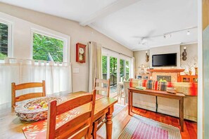 Ein Essbereich mit Holztisch und -stühlen, einem Korbfruchtkorb und Blick ins Freie durch große Fenster.