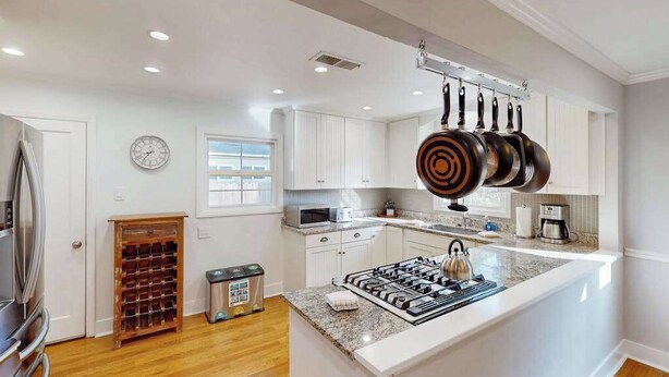 Una cocina moderna con armarios blancos, una isla central y una estructura colgante para ollas.