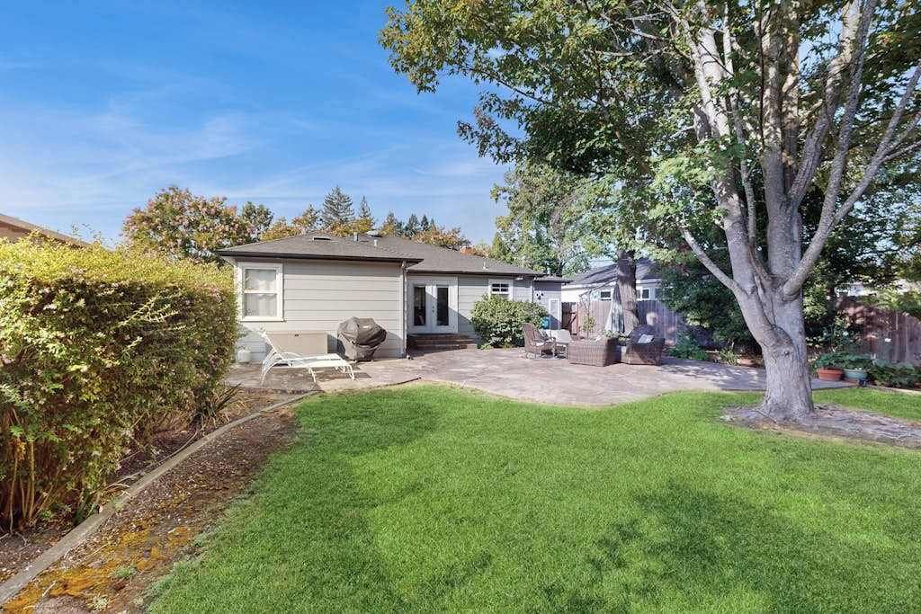 Una propiedad residencial con césped cuidado, un patio con mobiliario exterior y un árbol grande en el jardín.