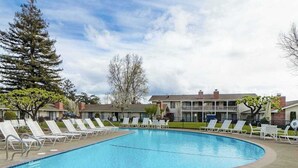 Una piscina con sillones de descanso, un edificio con balcón y árboles.