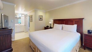 Habitación de hotel con una cama grande, una mesita de noche de madera, un escritorio con lámpara y un televisor.