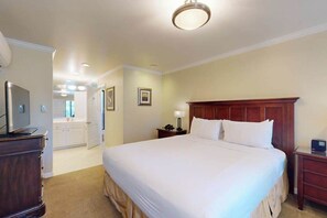 Ein Hotelzimmer mit einem großen Bett, einem Nachttisch aus Holz, einem Schreibtisch mit Lampe und einem Fernseher.