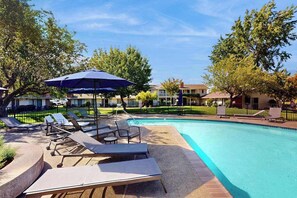 A swimming pool with lounge chairs and umbrellas, surrounded by trees and buildings.