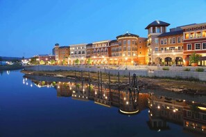 A waterfront hotel with multiple buildings, a reflection in the water, and a clear sky.
