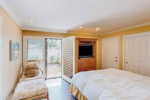 Une chambre à coucher comprenant un lit, une chaise, un téléviseur et une porte donnant sur un balcon.