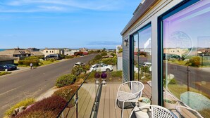 Un balcon avec des sièges d’extérieur, une vue sur une rue résidentielle et une grande porte vitrée.