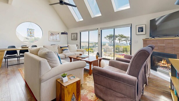 Un salon moderne doté d’une cheminée, d’un ventilateur de plafond et de grandes fenêtres.