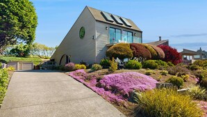 Une maison avec un toit en pente, de grandes fenêtres et un jardin bien entretenu, agrémenté de diverses plantes et fleurs.