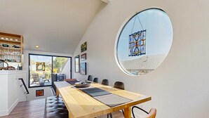 Un espace repas comprenant une longue table, des chaises, un banc, une fenêtre ronde et une vue sur l’extérieur.