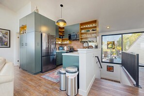 A modern kitchen with a built-in refrigerator, microwave, and stove. There is a dining area with a view of the outdoors. - Bodega Bay 2BR ocean-view home with pool table, on the golf course (Bodega Bay)