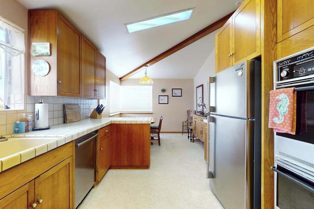A kitchen with wooden cabinets, a central island, stainless steel appliances, and a dining area with chairs.