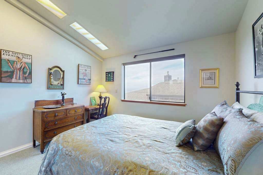 A bedroom with a bed, dresser, lamp, and a window with a view.