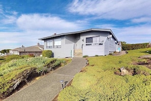 A single-story house with a front porch, a pathway leading to the entrance, and a grassy yard. - Bodega Bay 3BR hilltop home with panoramic ocean views & wraparound deck (Bodega Bay)
