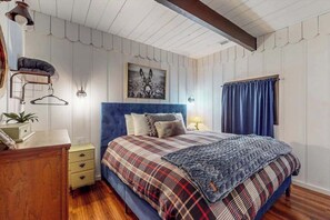 Ein Schlafzimmer mit einem Bett, einer Kommode, einem Nachttisch, einer Wandlampe und einem gerahmten Bild.