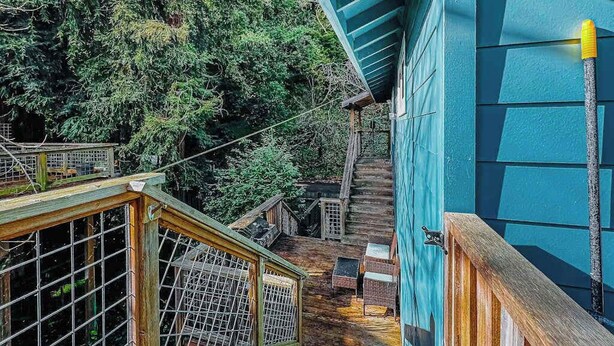 Eine Holztreppe führt zu einer Hütte mit blauer Fassade, umgeben von dichtem Wald.