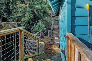 Un escalier en bois mène à un chalet à l’extérieur bleu, entouré d’une forêt dense.