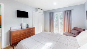 Ein Schlafzimmer mit Bett, Kommode, Fernseher und einer Glastür zum Außenbereich.
