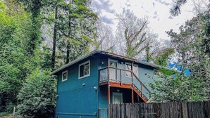Ein blaues Haus mit zwei Stockwerken, einer Holzterrasse und einem eingezäunten Garten.