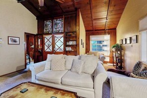A living room with a white sofa, wooden ceiling, and a bookshelf. - Guerneville 1BR + studio cabin near the river — small dogs welcome (Guerneville)