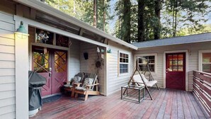 Eine Holzterrasse mit Sitzgelegenheiten im Freien, einer Schaukel und einem überdachten Eingangsbereich.