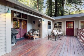 A wooden deck with outdoor seating, a swing, and a covered entryway. - Guerneville 1BR + studio cabin near the river — small dogs welcome (Guerneville)