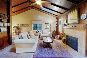 A spacious living room with a high ceiling, a fireplace, and a large window. - Guerneville 1BR + studio cabin near the river — small dogs welcome (Guerneville)