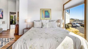 A bedroom with a large bed, a painting on the wall, and a view of the outside. - Bodega Bay 5BR ocean-view home with hot tub — dogs welcome (Bodega Bay)