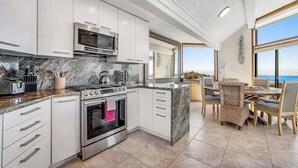 A modern kitchen with white cabinets, a built-in oven, and a dining area with wicker chairs. - Bodega Bay 5BR ocean-view home with hot tub — dogs welcome (Bodega Bay)