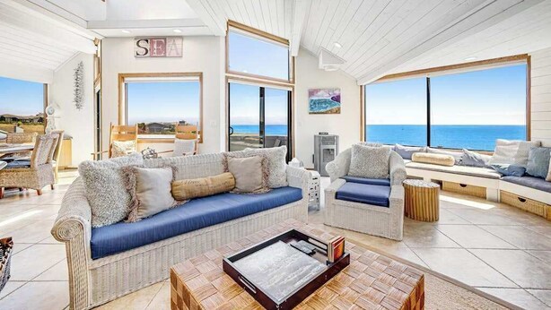 A spacious living area with a large window overlooking the sea, a sofa with cushions, and a coffee table. - Bodega Bay 5BR ocean-view home with hot tub — dogs welcome (Bodega Bay)