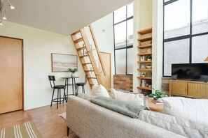 Un salon avec un canapé, une table basse, un téléviseur, une bibliothèque et une échelle appuyée contre le mur.
