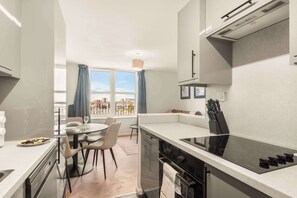 A modern kitchen with a built-in oven, a dining area with a table and chairs, and a view through a large window.
