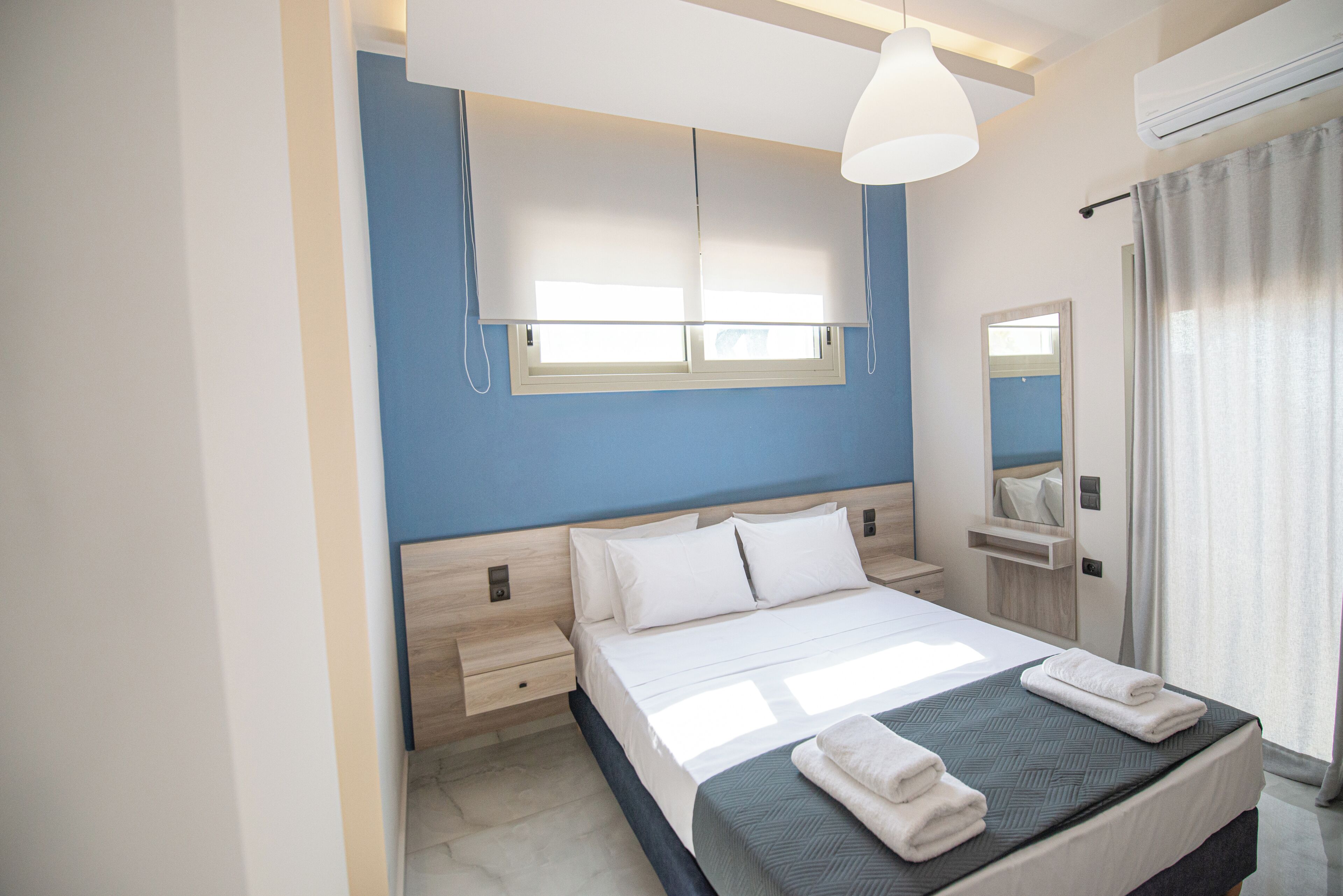 Ein modernes Schlafzimmer mit Bett, Nachttischen, einem Spiegel und einem Fenster mit Jalousien.