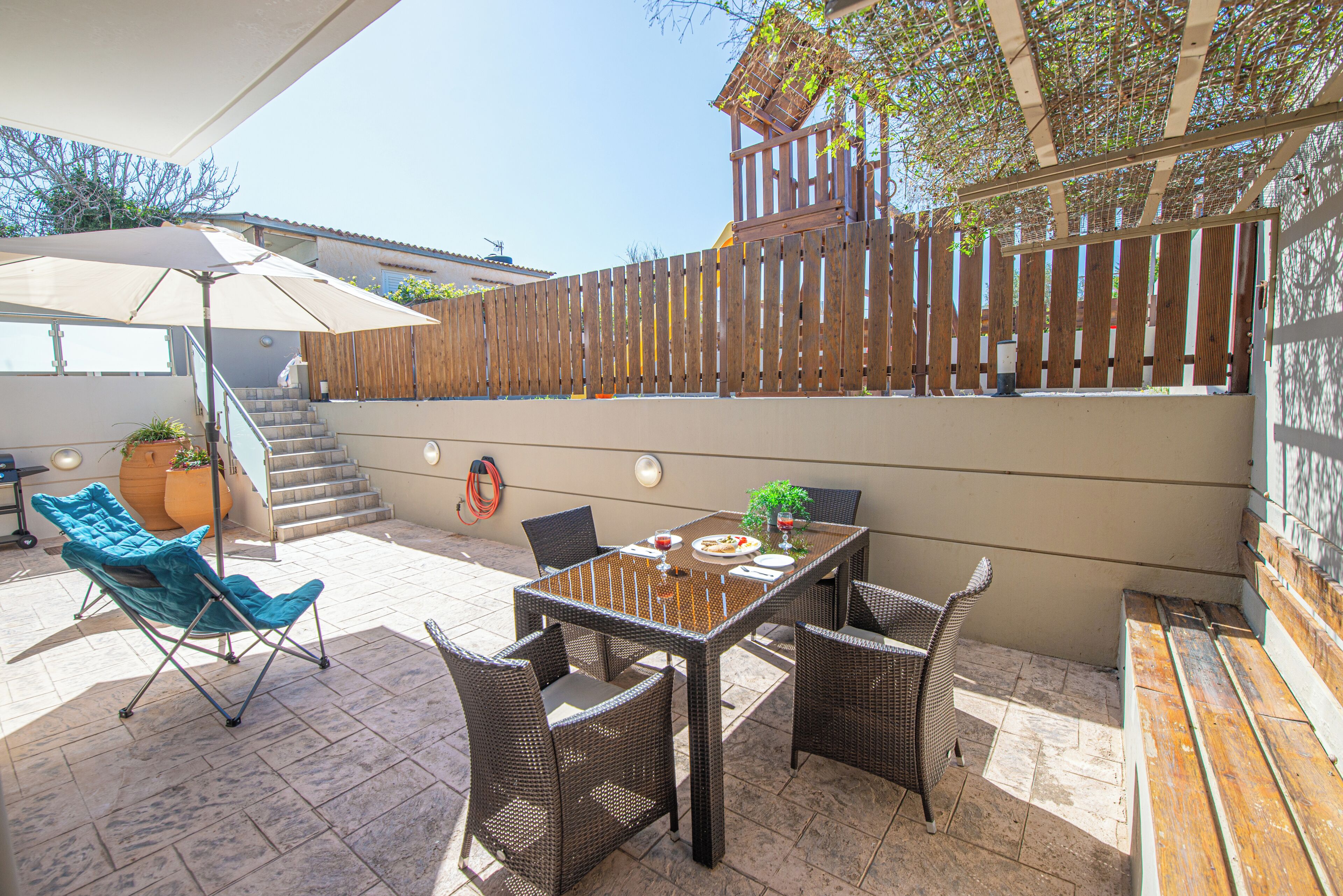 Une terrasse extérieure avec une table, des chaises, une chaise pliante et une clôture en bois.