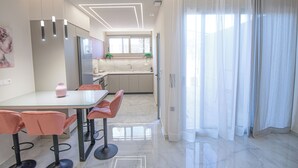 Eine moderne Küche mit Essbereich, inklusive Glastisch und Stühlen, einem Kühlschrank und einem Fenster mit Vorhängen.