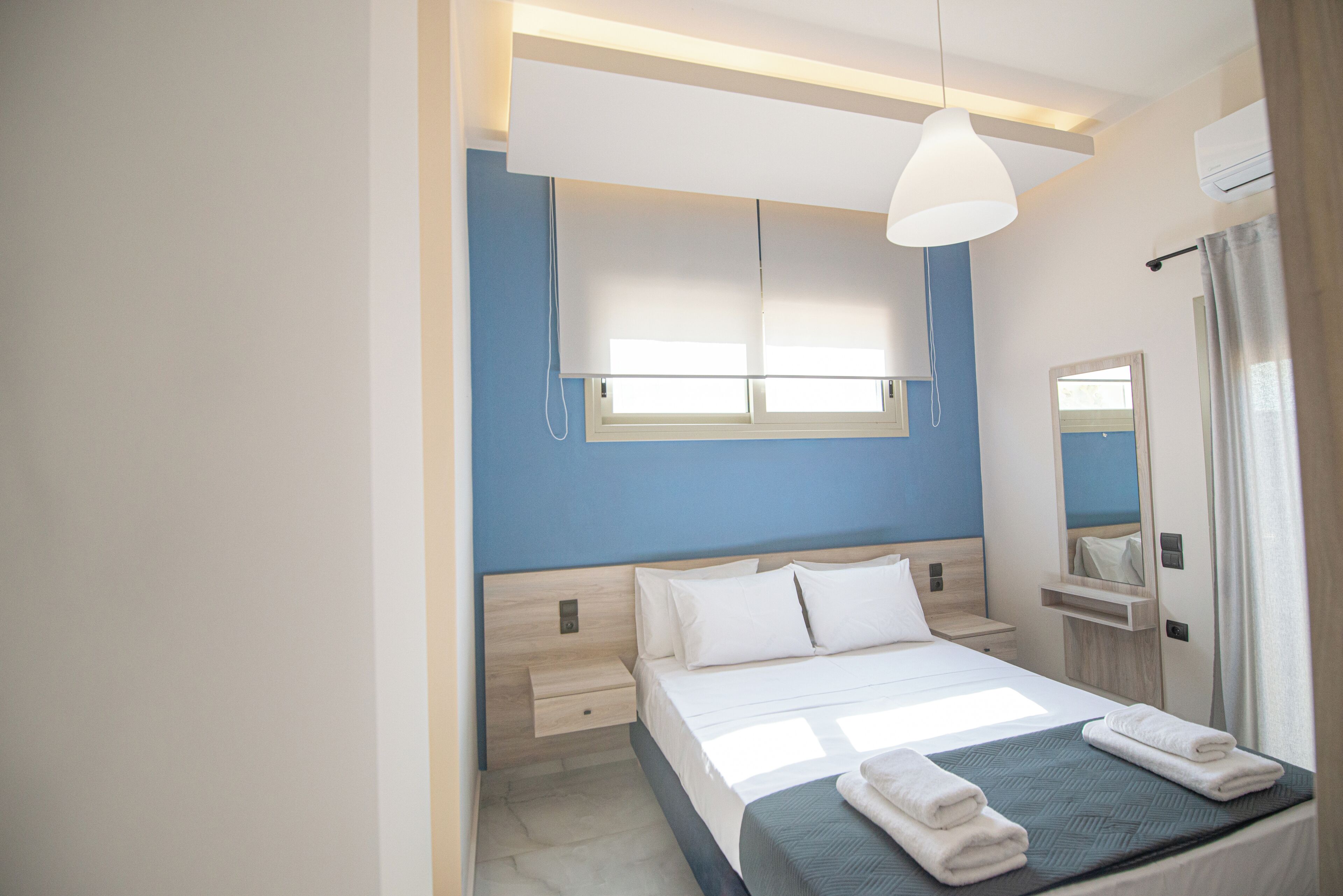 Een moderne hotelkamer met een bed, nachtkastjes, een raam met zonwering, een spiegel en een airconditioning.