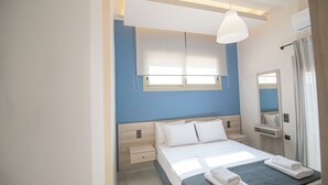 Ein modernes Hotelzimmer mit Bett, Nachttischen, einem Fenster mit Jalousien, einem Spiegel und einer Klimaanlage.