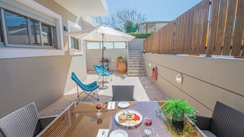 Une terrasse avec une table dressée pour le repas, des chaises d’extérieur, une plante en pot et une clôture en bois.
