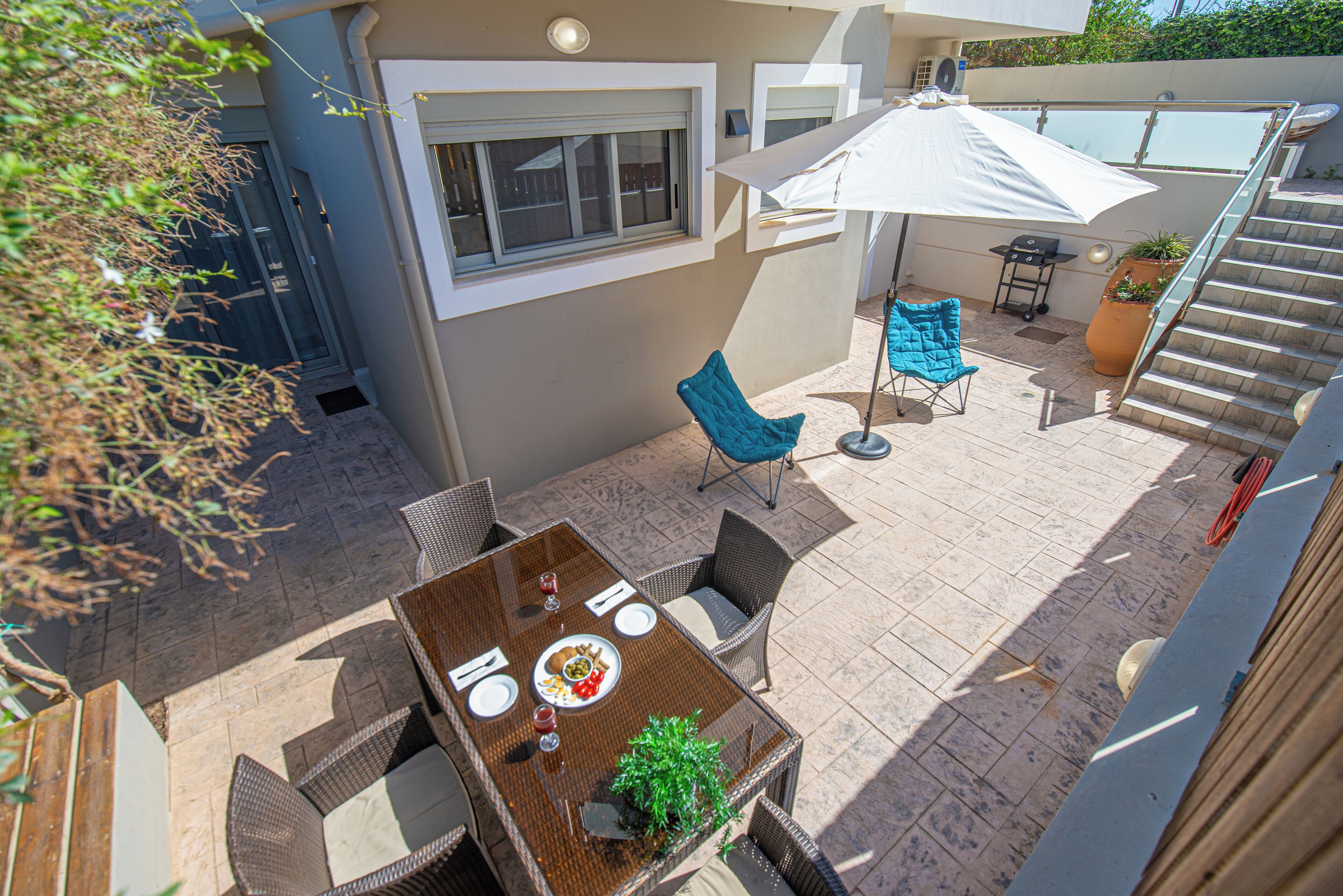 A patio with a table set for two, a chair, a potted plant, and a staircase leading to an upper level.