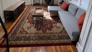 Ein Wohnzimmer mit einer Couch, einem Fernseher, einem Schreibtisch und einem gemusterten Teppich.