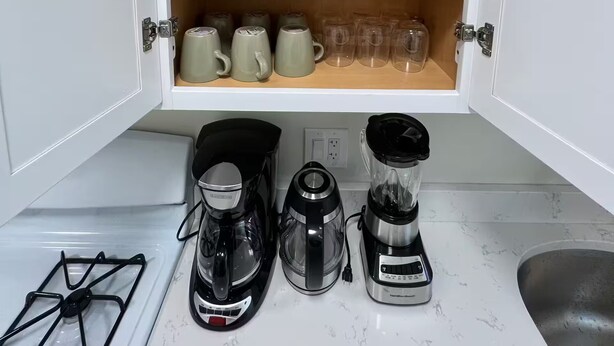 Eine Küche mit einem Schrank, der Tassen, eine Kaffeemaschine und einen Mixer beherbergt.