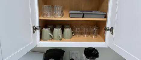 A kitchen with a cabinet containing mugs, a coffee maker, and a blender.