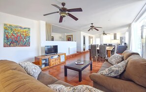 Un salon spacieux équipé d’un téléviseur, de canapés, d’une table basse et de ventilateurs de plafond.
