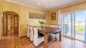 Un comedor con una mesa de madera, sillas de mimbre, un jarrón de flores y un cuadro en la pared.