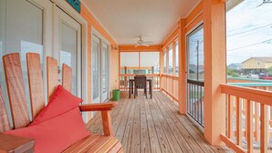 Une terrasse en bois avec une table et des chaises, un ventilateur de plafond et de grandes fenêtres.