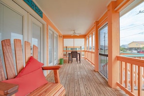 Eine Holzterrasse mit Tisch, Stühlen, einem Deckenventilator und großen Fenstern.