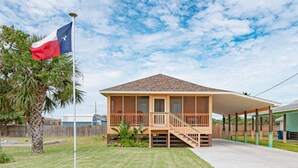 Une maison de plain-pied avec un porche, un mât sur lequel flotte un drapeau du Texas, et un ciel dégagé.